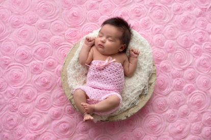 Portrait of a sleeping, one month old baby girl wearing a crocheted, pink romper.