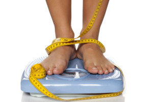 woman's feet on a domestic weight scale and measuring tape around them